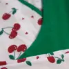 Pyjama doux en coton blanc à motifs de cerises, avec finition vert émeraude, idéal pour une tenue d'intérieur confortable.