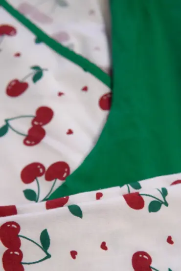 Pyjama doux en coton blanc à motifs de cerises, avec finition vert émeraude, idéal pour une tenue d'intérieur confortable.