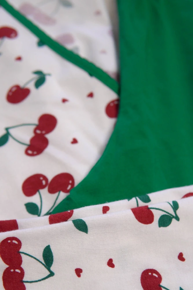 Pyjama doux en coton blanc à motifs de cerises, avec finition vert émeraude, idéal pour une tenue d'intérieur confortable.