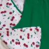 Pyjama doux en coton, motif cerises sur fond blanc, avec un pantalon vert, idéal pour une tenue d'intérieur confortable.