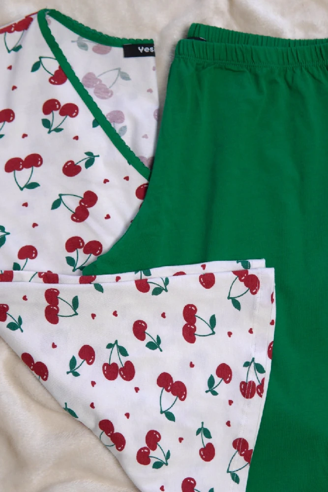 Pyjama doux en coton, motif cerises sur fond blanc, avec un pantalon vert, idéal pour une tenue d'intérieur confortable.