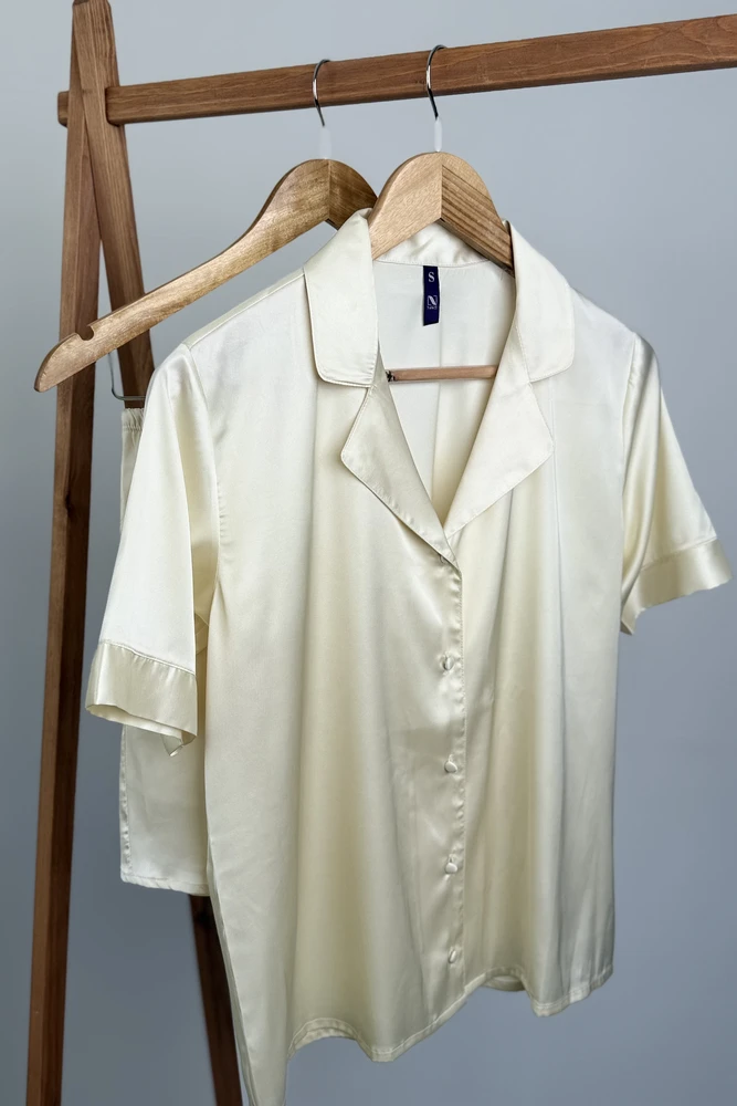 Pyjama satin élégant couleur crème, en tissu doux et léger, parfait pour une tenue d'intérieur confortable et raffinée.